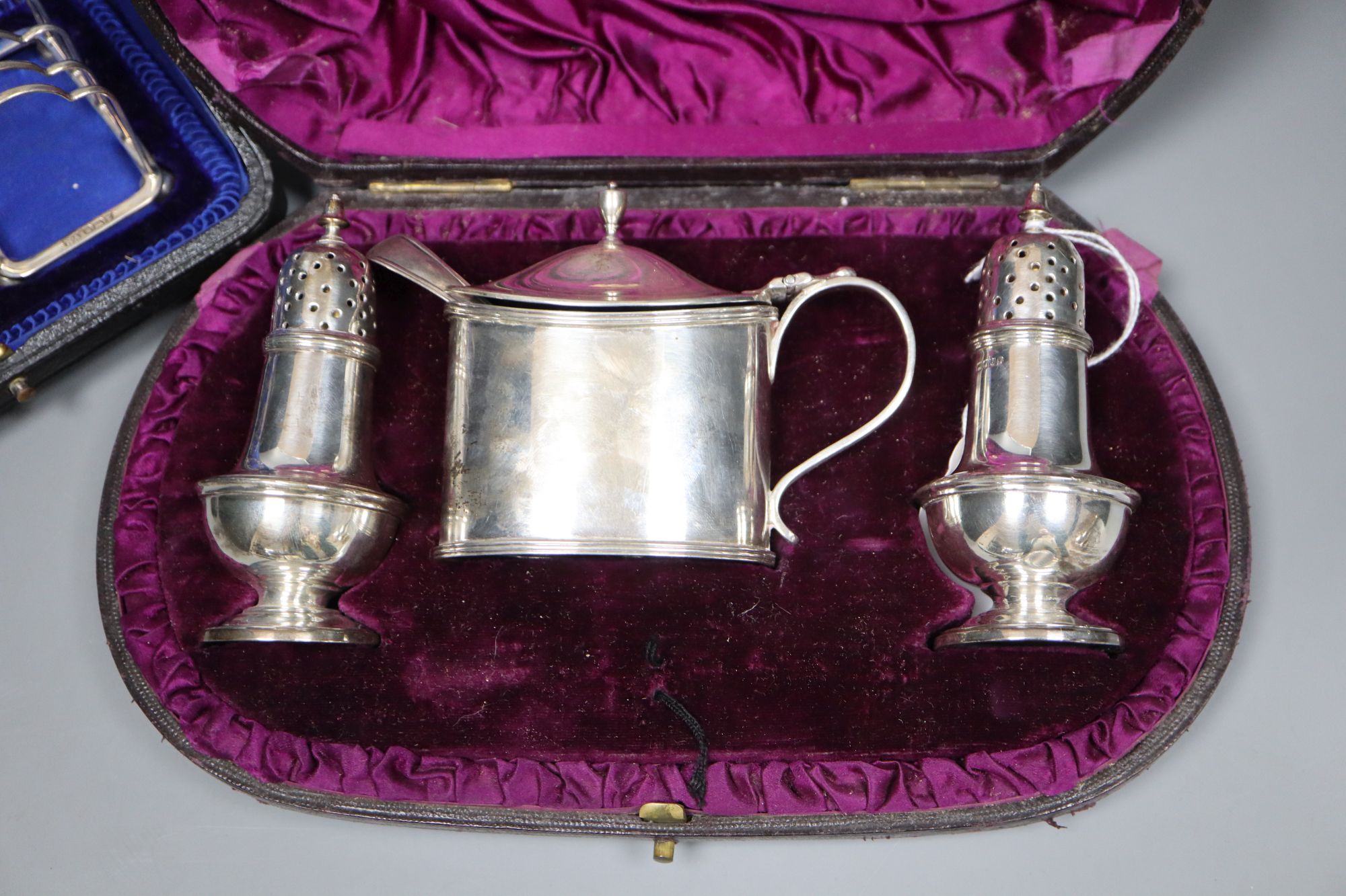 A Victorian silver three-piece condiment set, London, 1882, cased and a pair of small Edwardian silver toast racks, cased.